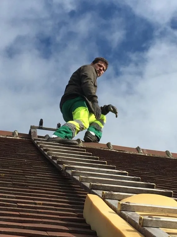L'artisan Beautour sur un toit de tuiles, échelle de couvreur posée sur la pente, avant l'entretien de la couverture