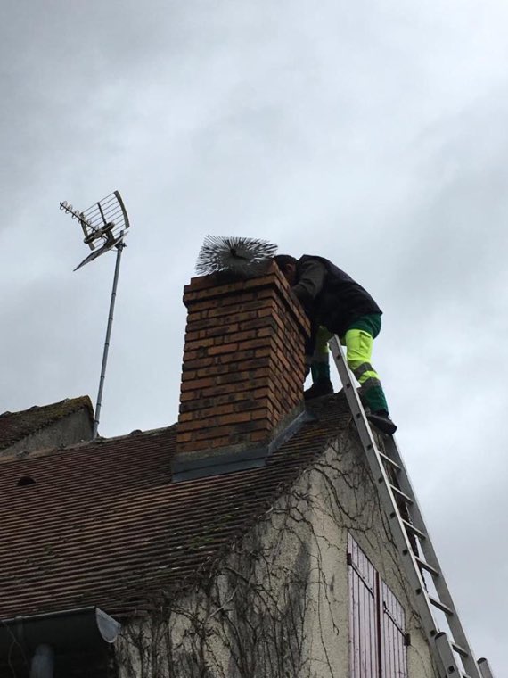 Ramoneur en haut d'une échelle brossant une souche de cheminée en brique avec un hérisson
